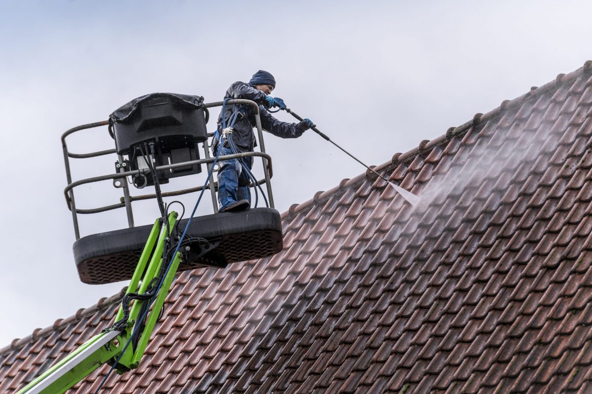 dak schoonmaken met hogedrukreiniger vanaf een hoogwerker